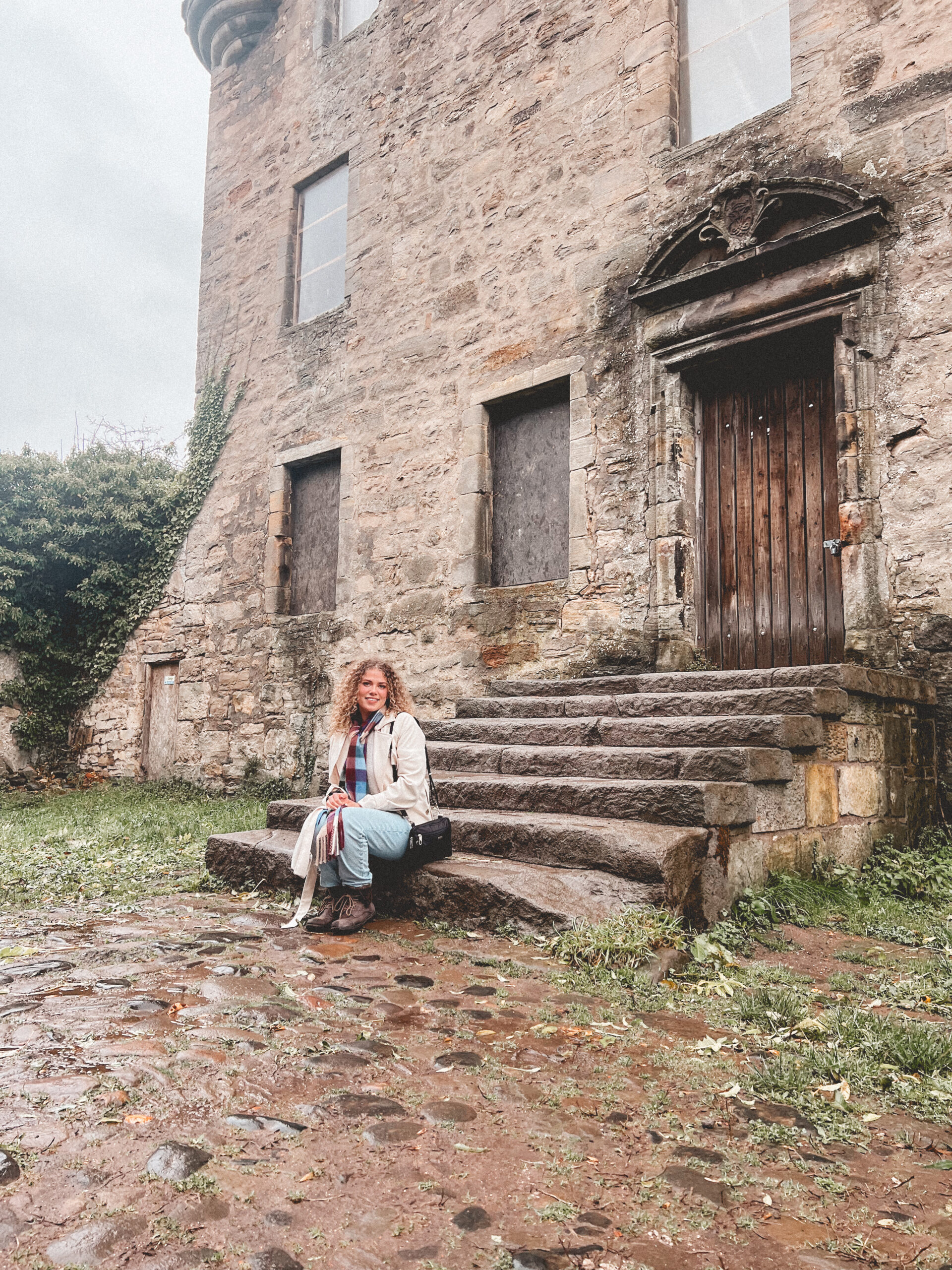 Woman sitting on the steps of Midhope Castle in Scotland, used as an Outlander filming location as Lallybroch.